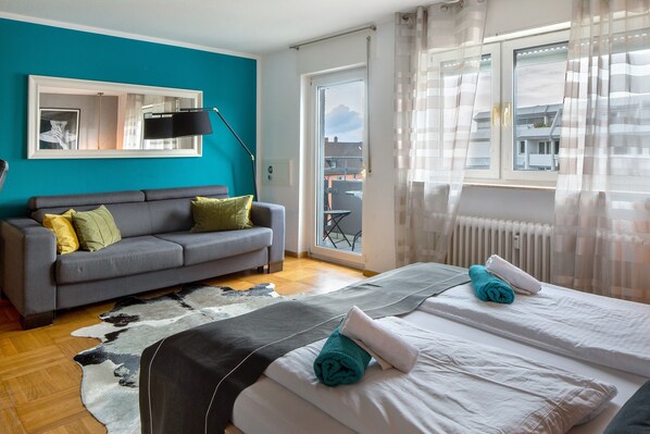 A bedroom with a bed, a grey sofa, a cowhide rug, and a view through a window.