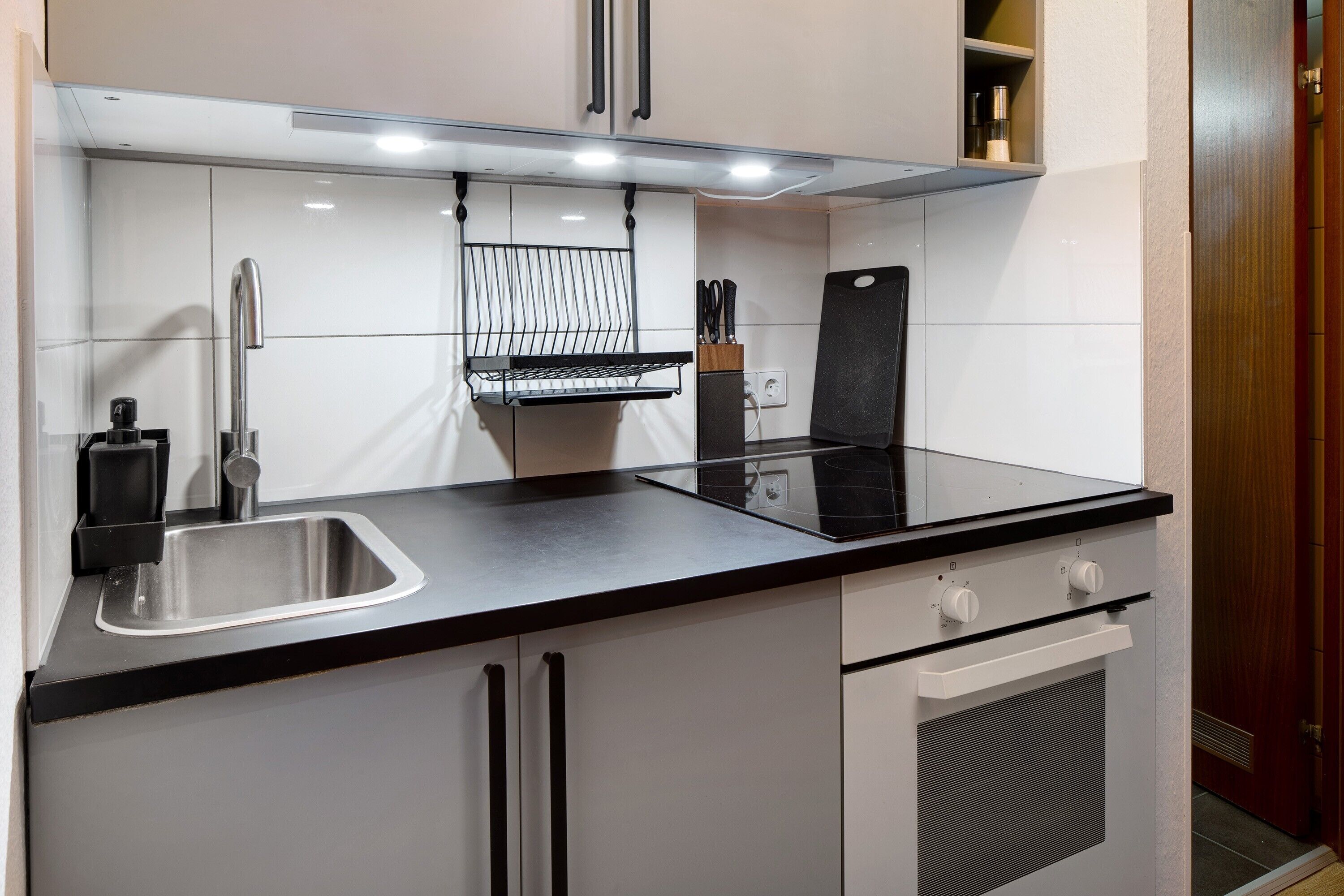 A modern kitchen with a stainless steel sink, black countertop, white cabinets, and a built-in oven.