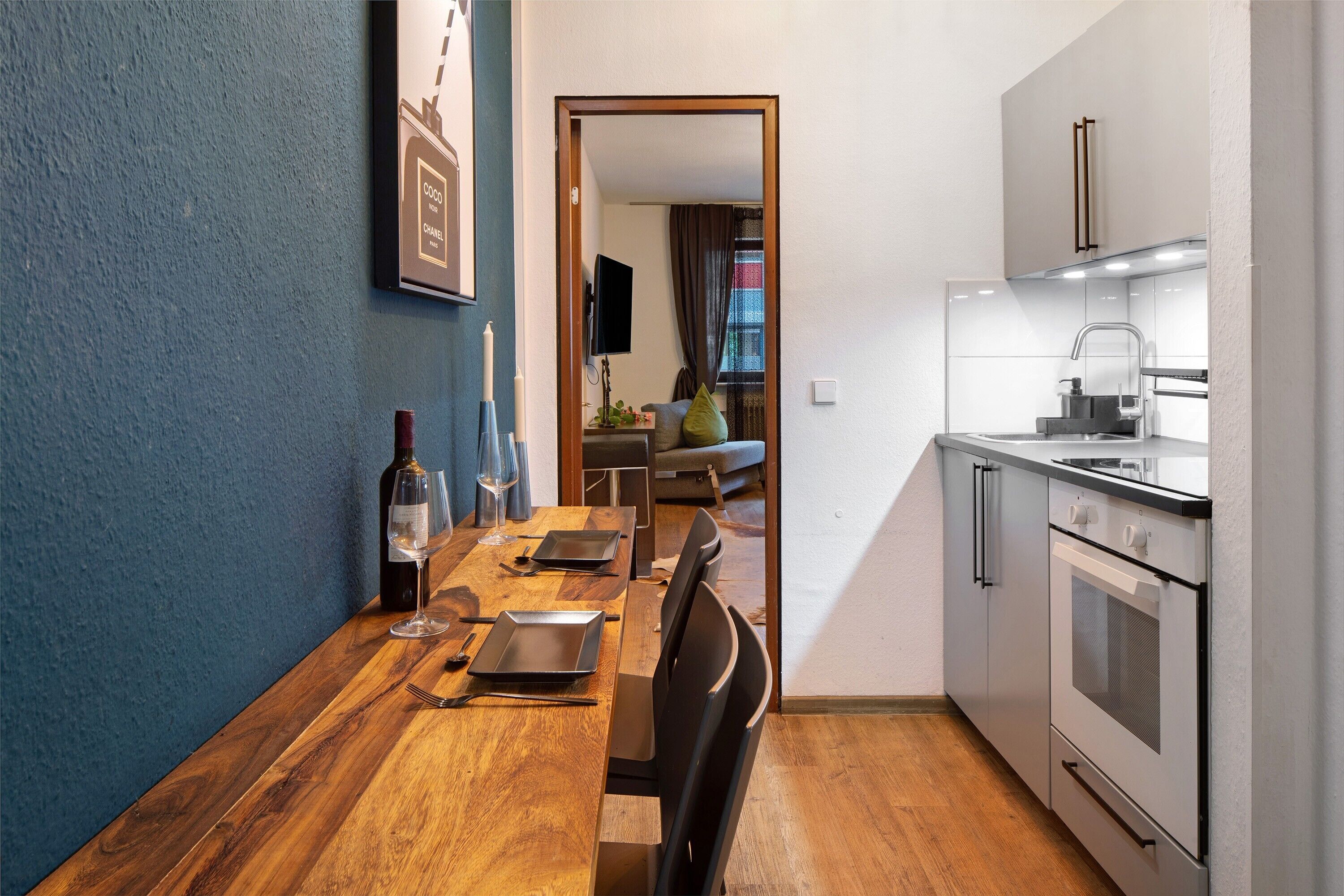 Een moderne keuken met een houten eettafel, een inbouwoven en een televisie op de achtergrond.