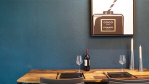A dining table with a bottle of wine, two glasses, and a framed picture of a perfume bottle. - Holiday Apartment 'Am Bahnhof Freiburg' with Wi-Fi (Freiburg im Breisgau)