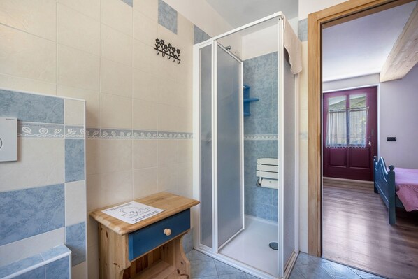 A bathroom with a shower, a wooden cabinet, and a tiled wall.