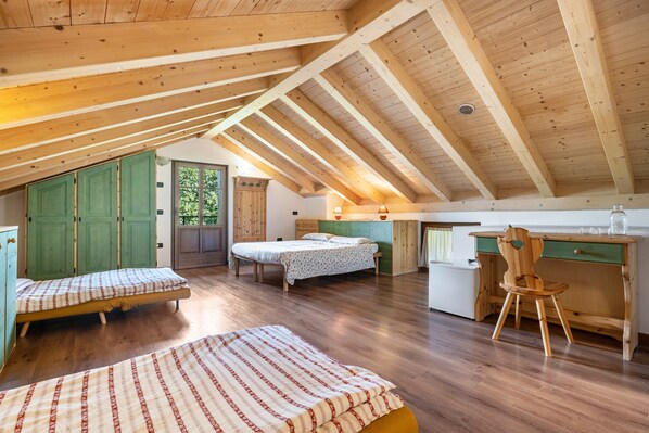 A loft-style bedroom with wooden beams, two beds, a desk, and a chair.