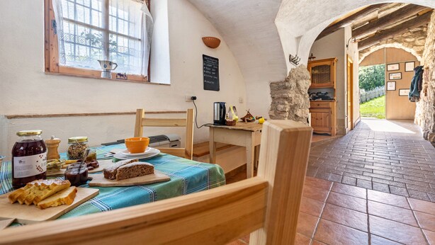A rustic kitchen with a table set for breakfast, a window with curtains, and a stone wall.