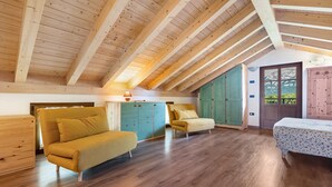 A spacious loft with wooden beams, a sofa, a chair, and a bed.
