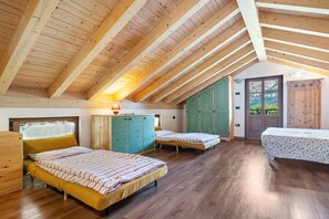 A room with wooden beams, two beds, a wardrobe, and a door leading outside.