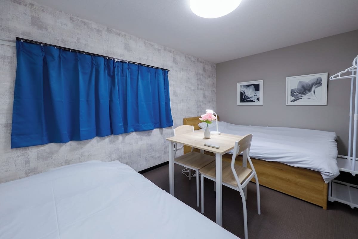 A bedroom with two beds, a desk with a chair, and a window with blue curtains.