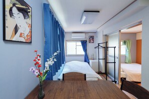 A compact hotel room with a bed, a small table, a vase with flowers, a wall-mounted air conditioner, and a sliding door leading to another room. - Grace Heiwajima (Tokyo)