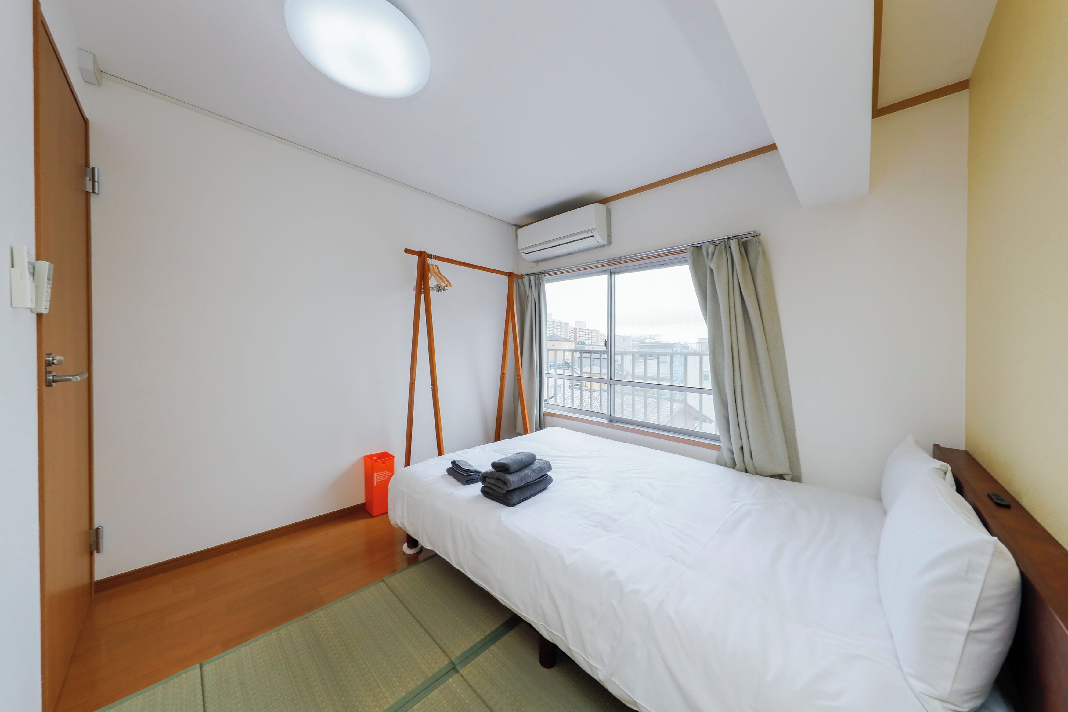 Une chambre d’hôtel avec un lit, une fenêtre avec des rideaux, un appareil de climatisation et un plancher en bois.