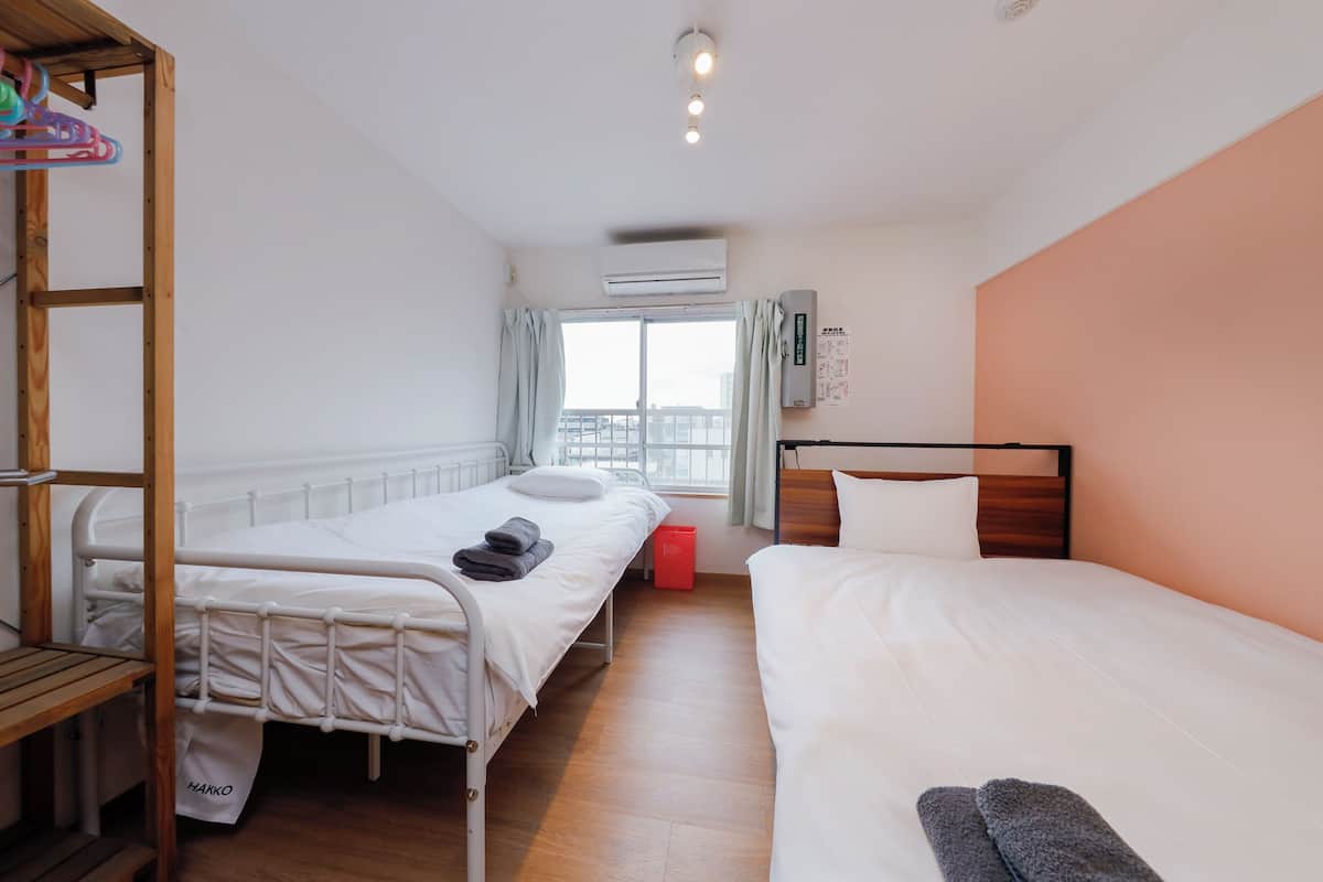 A hotel room with two beds, a wooden shelf, an air conditioning unit, and a window with curtains.