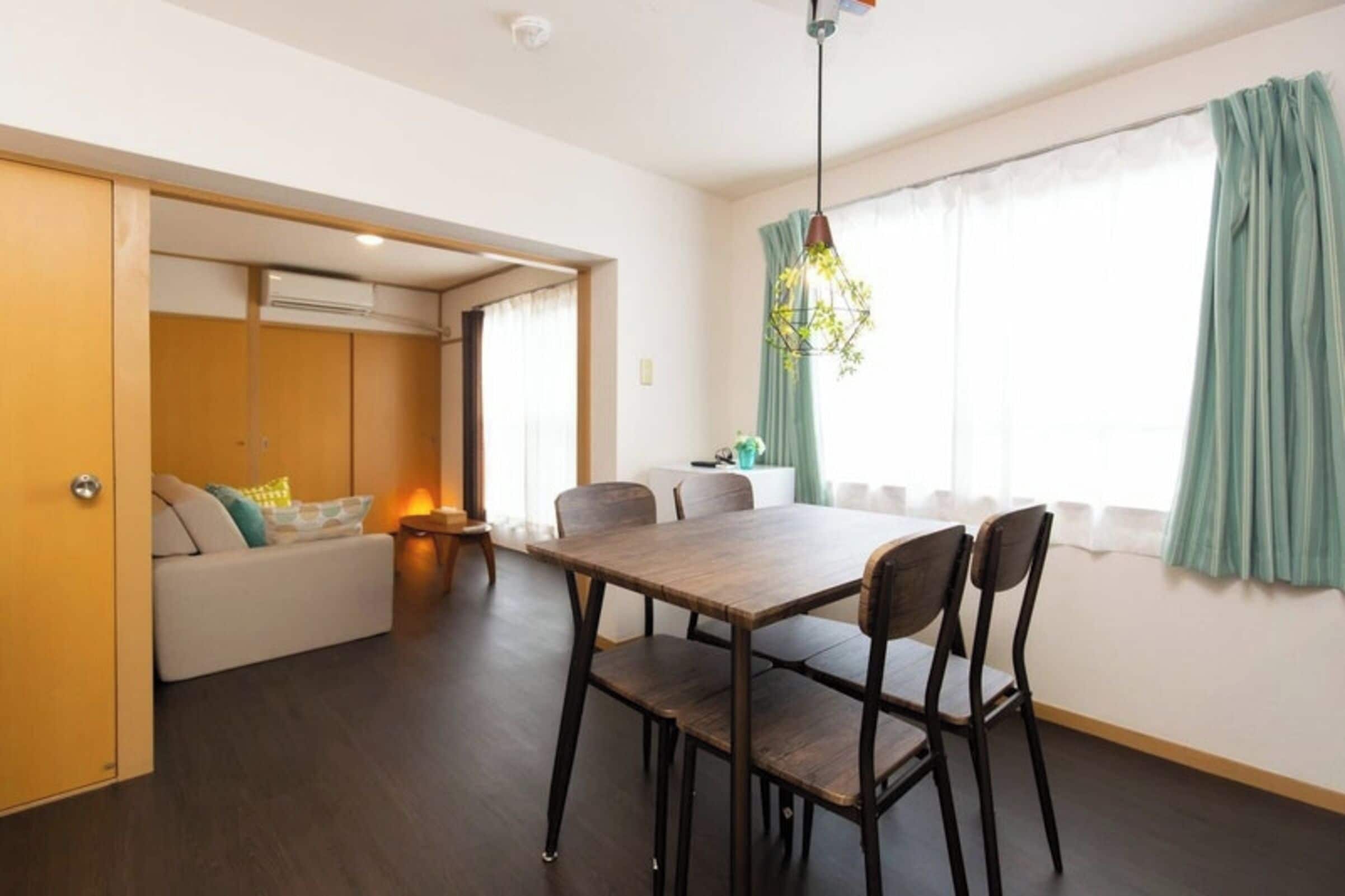 A modern living room with a dining area, a sofa, a table, and a hanging light fixture.