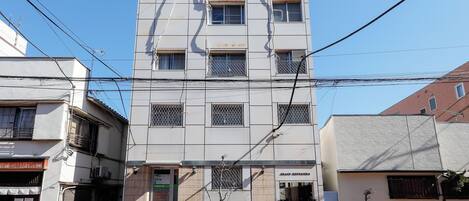 Un immeuble à plusieurs étages, doté d’une façade sobre, de nombreuses fenêtres et d’un petit hall d’entrée agrémenté de plantes en pot.