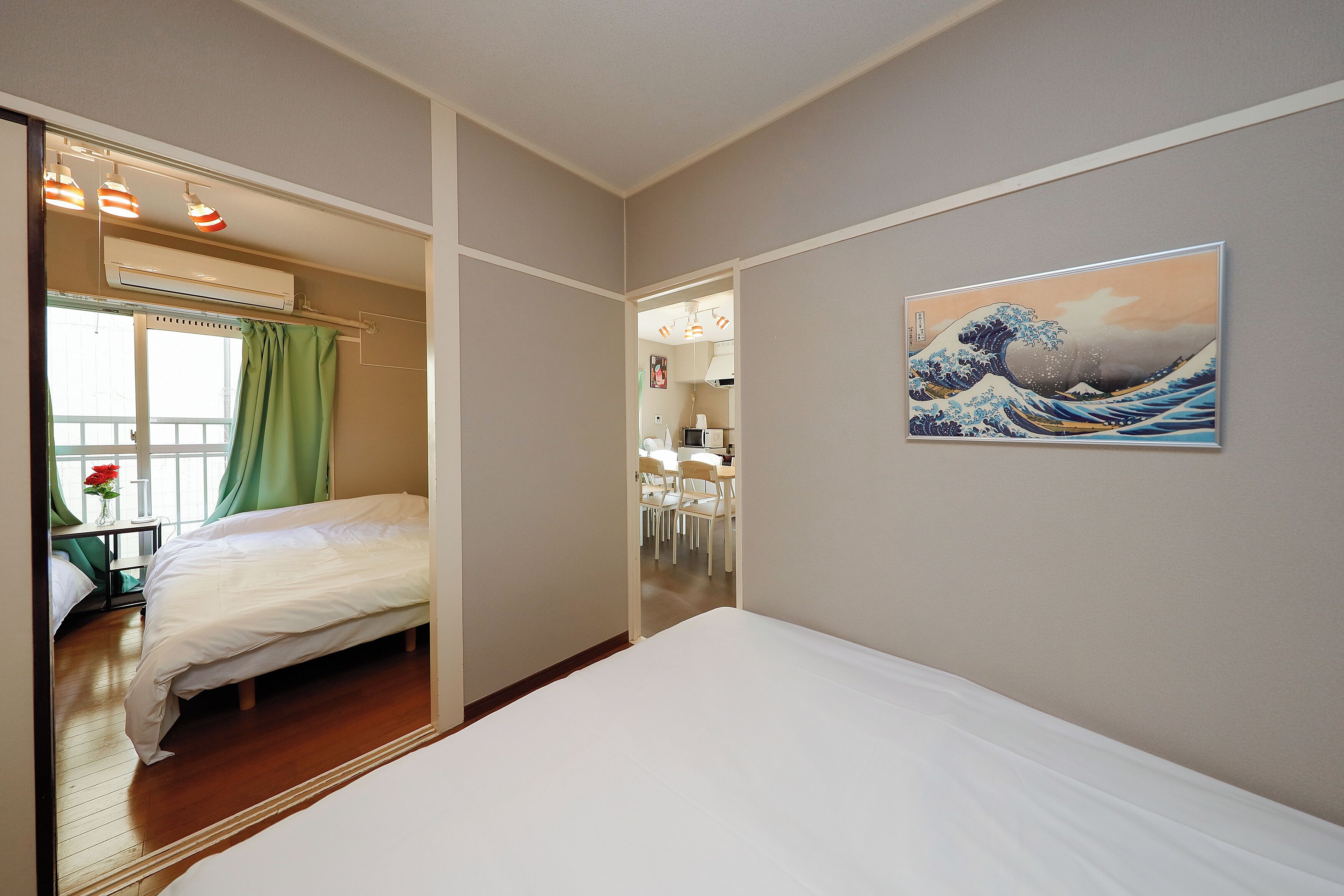 A hotel room with a bed, a painting, and a view of a dining area.