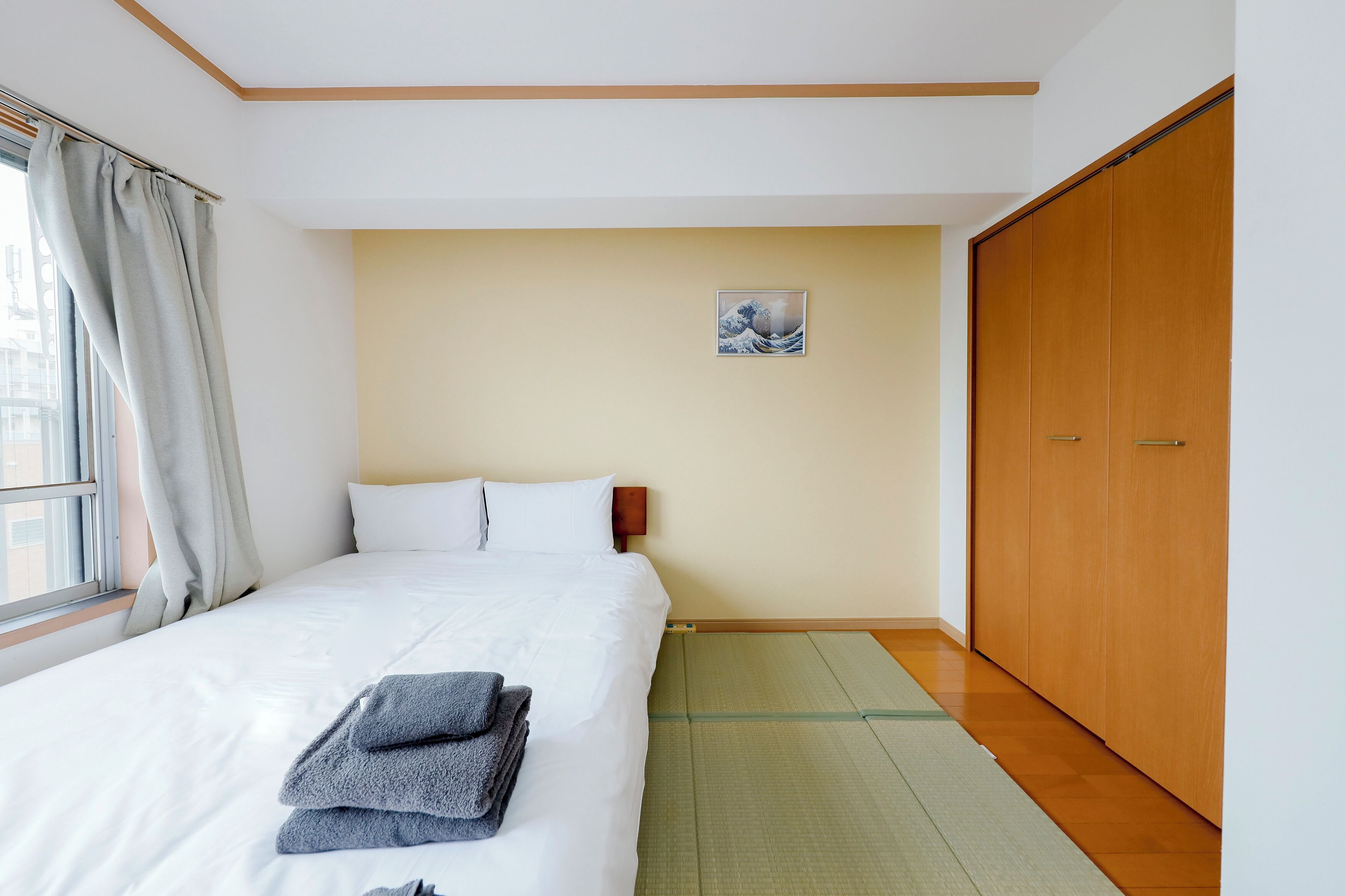 A hotel room with a bed, a wooden wardrobe, a window with curtains, and a tatami mat floor.