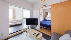 A modern hotel room with a large TV, a sofa, a bed, and a small table with remotes. - Grace Heiwajima (Tokyo)