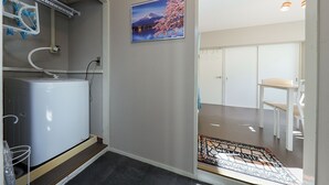 A compact kitchen with a built-in refrigerator, a drying rack, and a welcome mat at the entrance. - Grace Heiwajima (Tokyo)