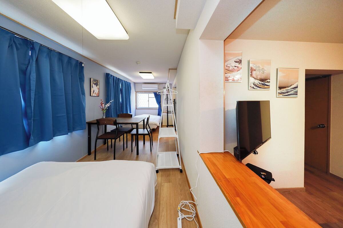 A hotel room with a bed, a desk, a chair, a TV, and artwork on the wall.