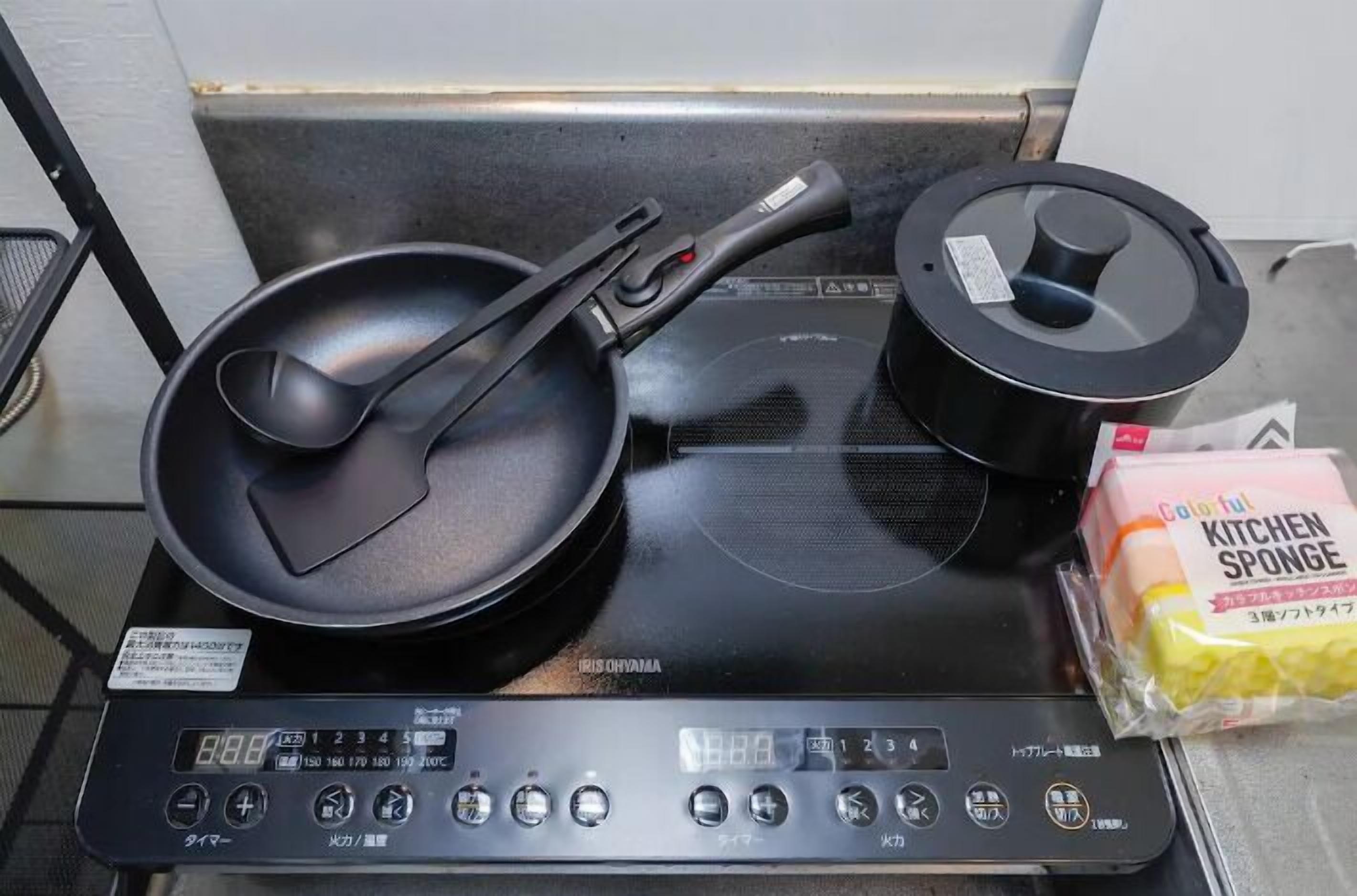 Een keuken met een fornuis, een koekenpan, een pan en een pak keukenpons.