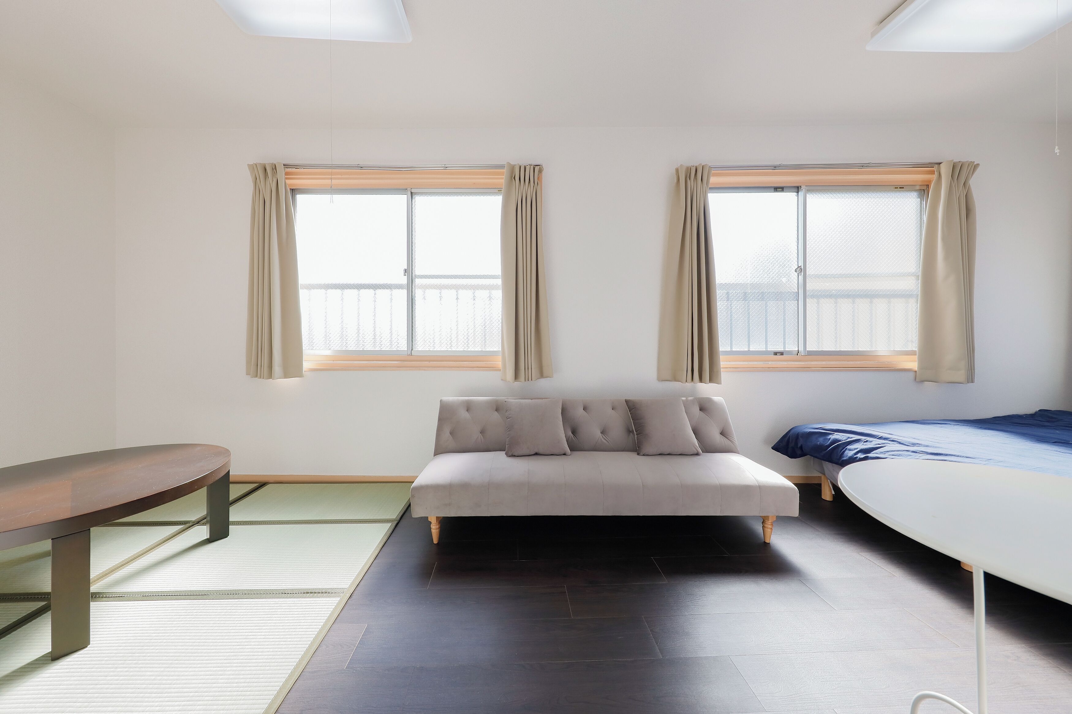 A room with a sofa, a bed, a bench, and two windows with curtains.