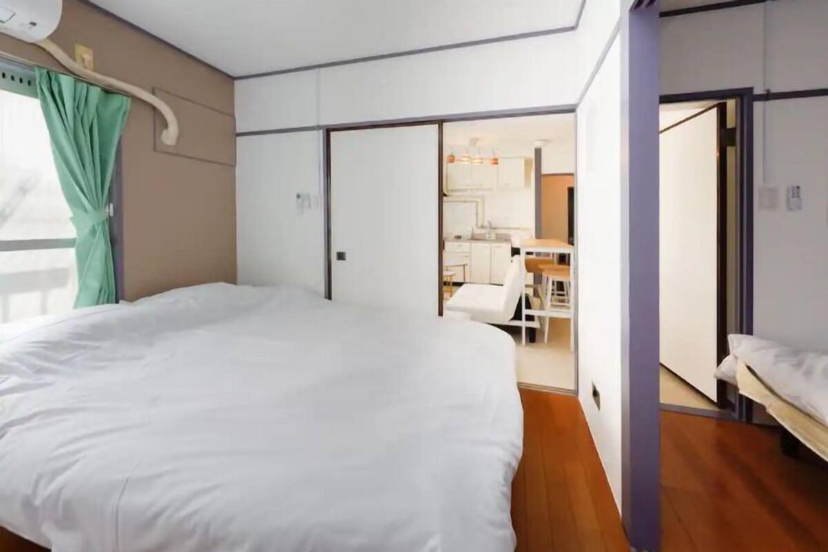 A bedroom with a large bed, a bathroom with a shower, and a kitchenette area.