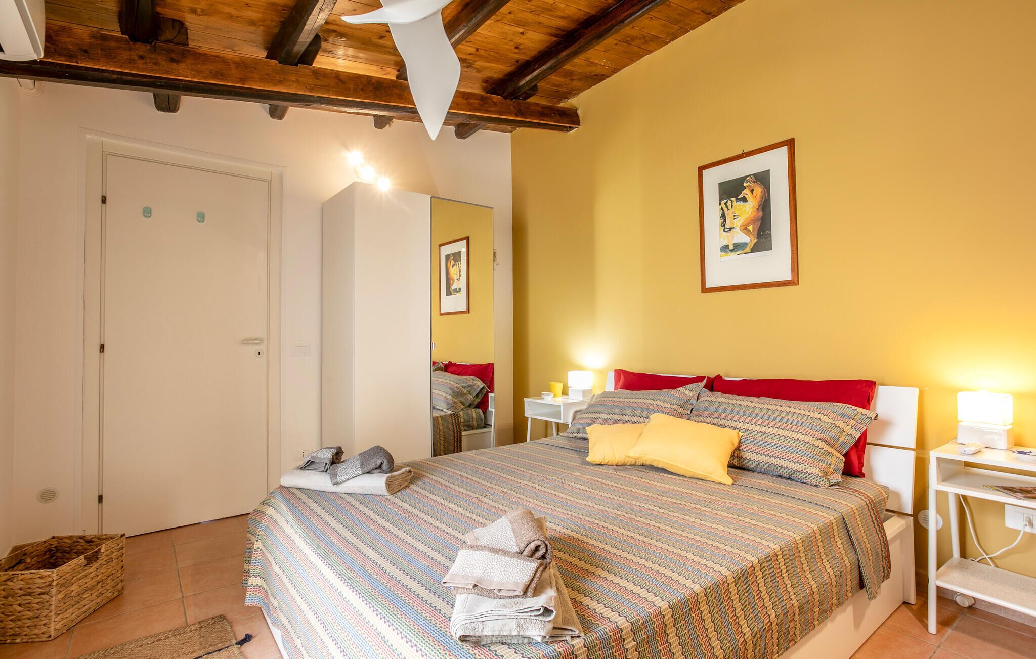 Une chambre à coucher avec un lit, des tables de chevet, un miroir et un tableau encadré au mur.