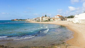 Une scène de plage côtière avec une eau bleue et limpide, un rivage sablonneux et des bâtiments dotés de balcons donnant sur la mer.
