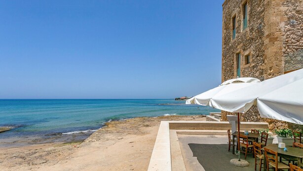 Un restaurant en bord de mer avec une terrasse, un bâtiment en pierre et une vue sur l’océan.