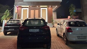 Ein zweistöckiges Hotel namens "Wings Grand" mit moderner Fassade, einem sichtbaren Eingang und zwei parkenden Autos davor.