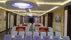 Ein Hotelkonferenzraum mit Reihen weißer Stühle, roter Tische und einer großen Kronleuchter.