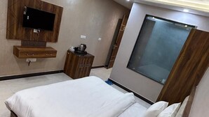 A modern bedroom with a large bed, a ceiling fan, a mounted TV, and a window. - Hotel Wings Grand (Alwar)