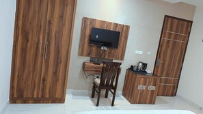 Una stanza con un'armadio in legno, una scrivania con una sedia, una televisione a parete e un mobiletto con una macchina da caffè.