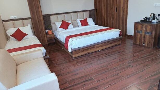 A hotel room with a large bed, a sofa, a wooden cabinet, and a potted plant. - Hotel Wings Grand (Alwar)