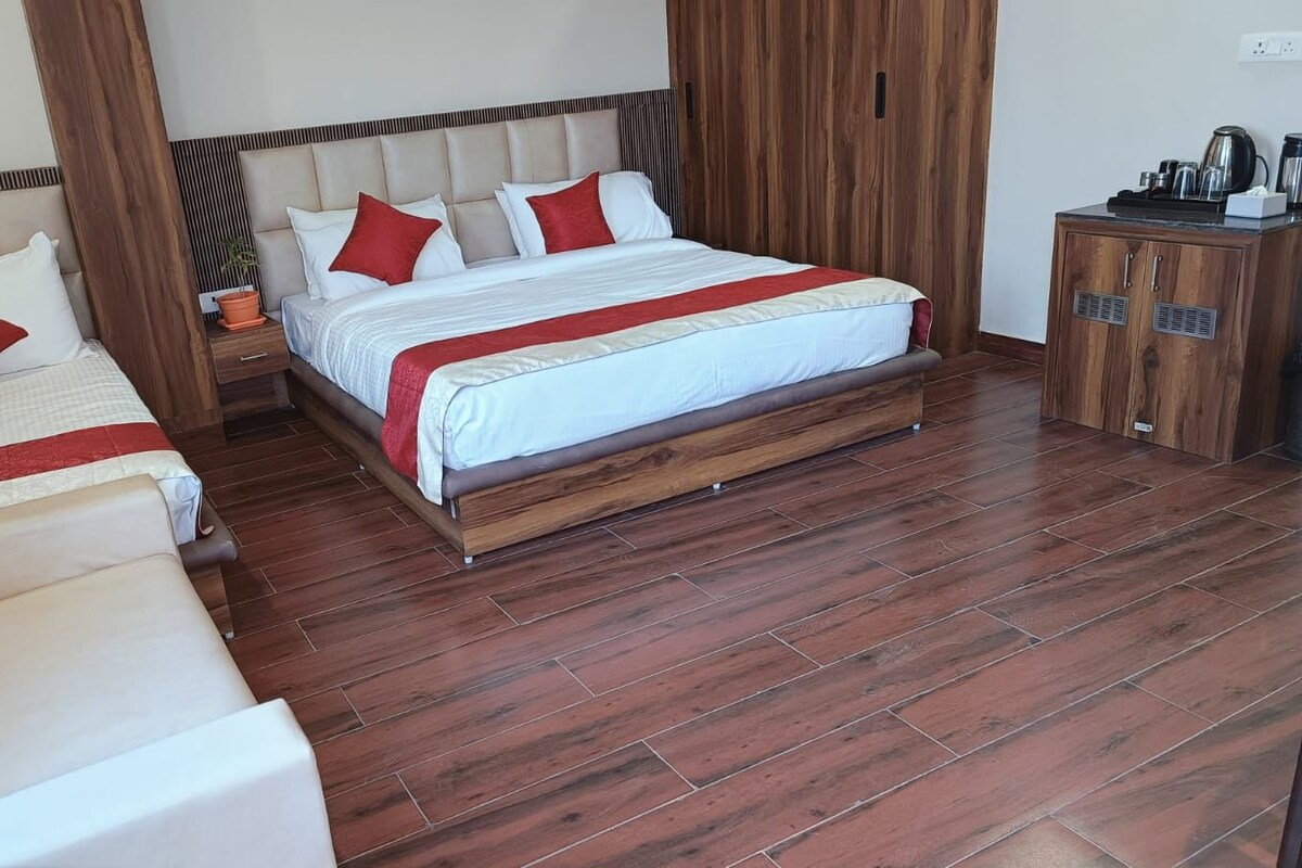 A hotel room with a large bed, a sofa, a wooden cabinet, and a potted plant.