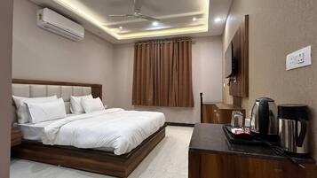 A hotel room with a bed, a desk with a coffee maker, and an air conditioner.