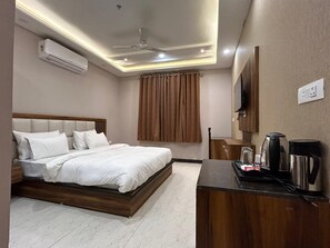 A hotel room with a bed, a desk with a coffee maker, and an air conditioner. - Hotel Wings Grand (Alwar)
