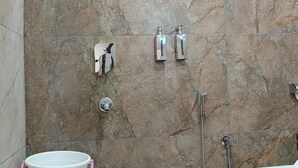 A bathroom with a shower, toilet, and a bucket. - Hotel Wings Grand (Alwar)