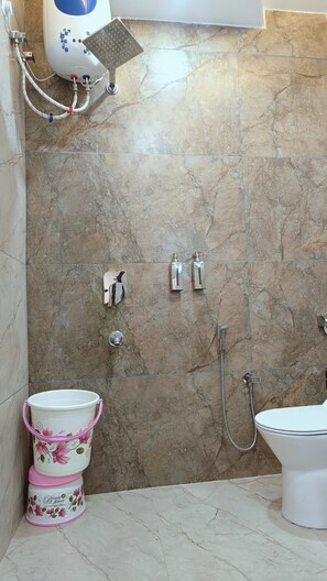 A bathroom with a shower, toilet, and a bucket. - Hotel Wings Grand (Alwar)