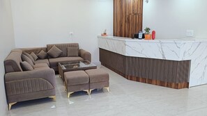 A modern living room with a sectional sofa, a glass coffee table, and a wooden accent wall. - Hotel Wings Grand (Alwar)