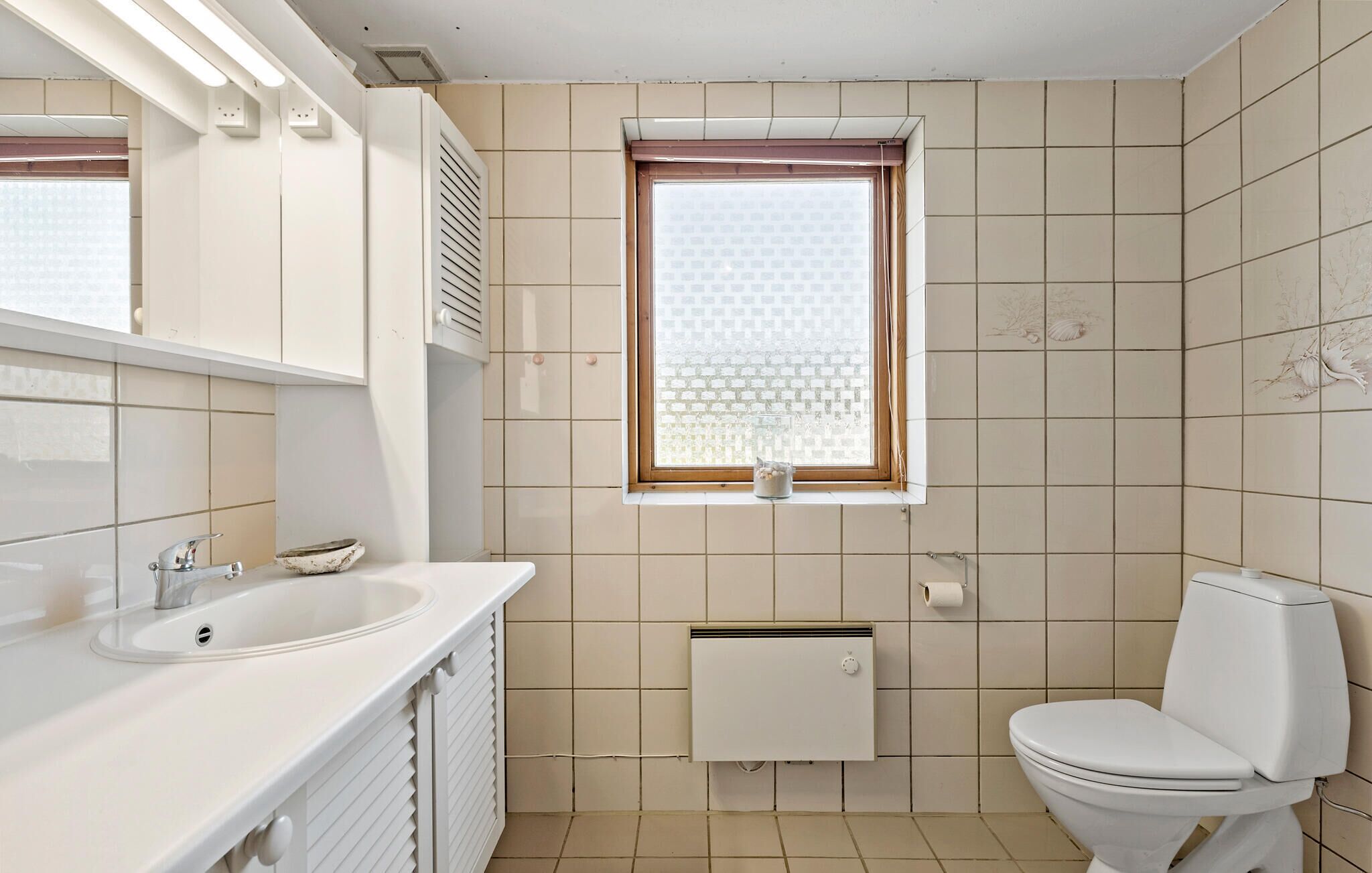 Een badkamer met een wit wastafelmeubel, toilet en raam met zonwering.