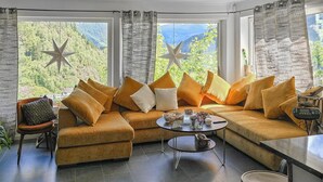 Ein gemütliches Wohnzimmer mit einer großen Couch, einem Couchtisch und Blick auf Berge durch große Fenster.