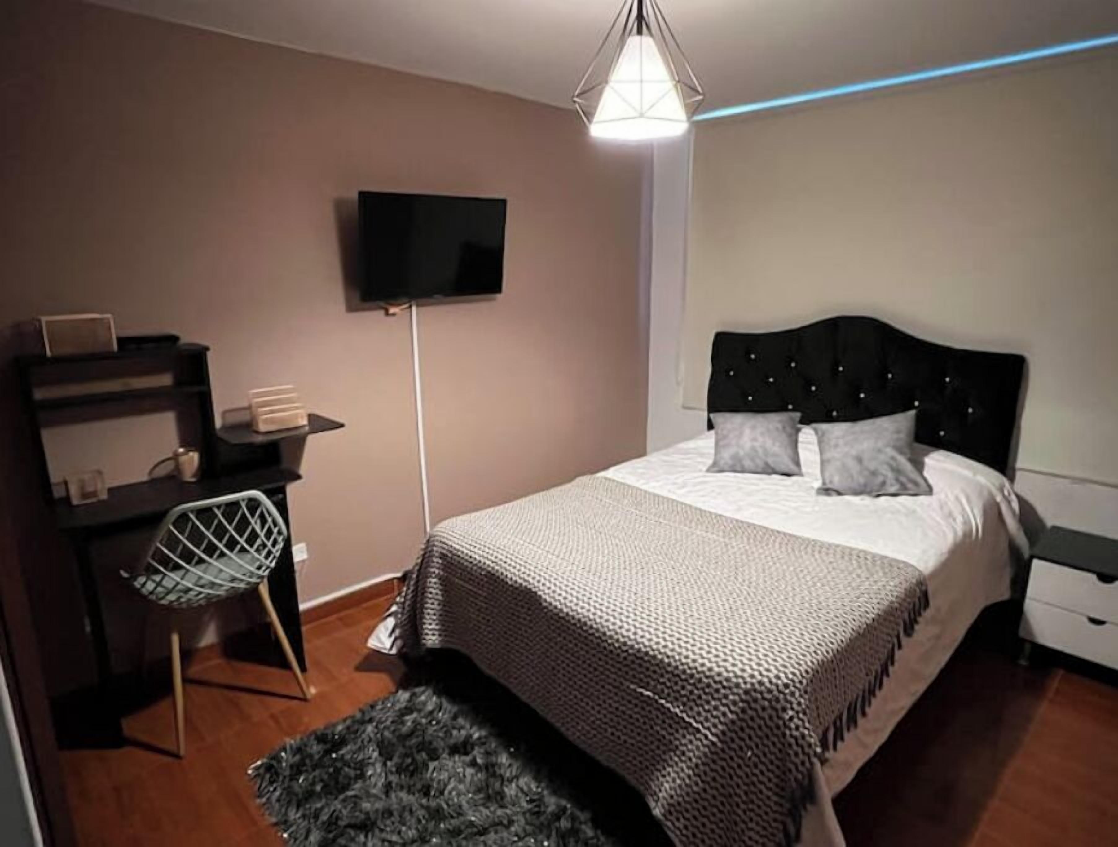 Ein Schlafzimmer mit einem Bett, einem Schreibtisch, einem Stuhl, einem Fernseher und einer Hängelampe.
