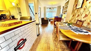 A kitchen with a brick backsplash, a dining area with a wooden table and chairs, and a living room with a sofa and a TV. - Shepherds Bush W12 Magical Townhouse nr Westfield (London)