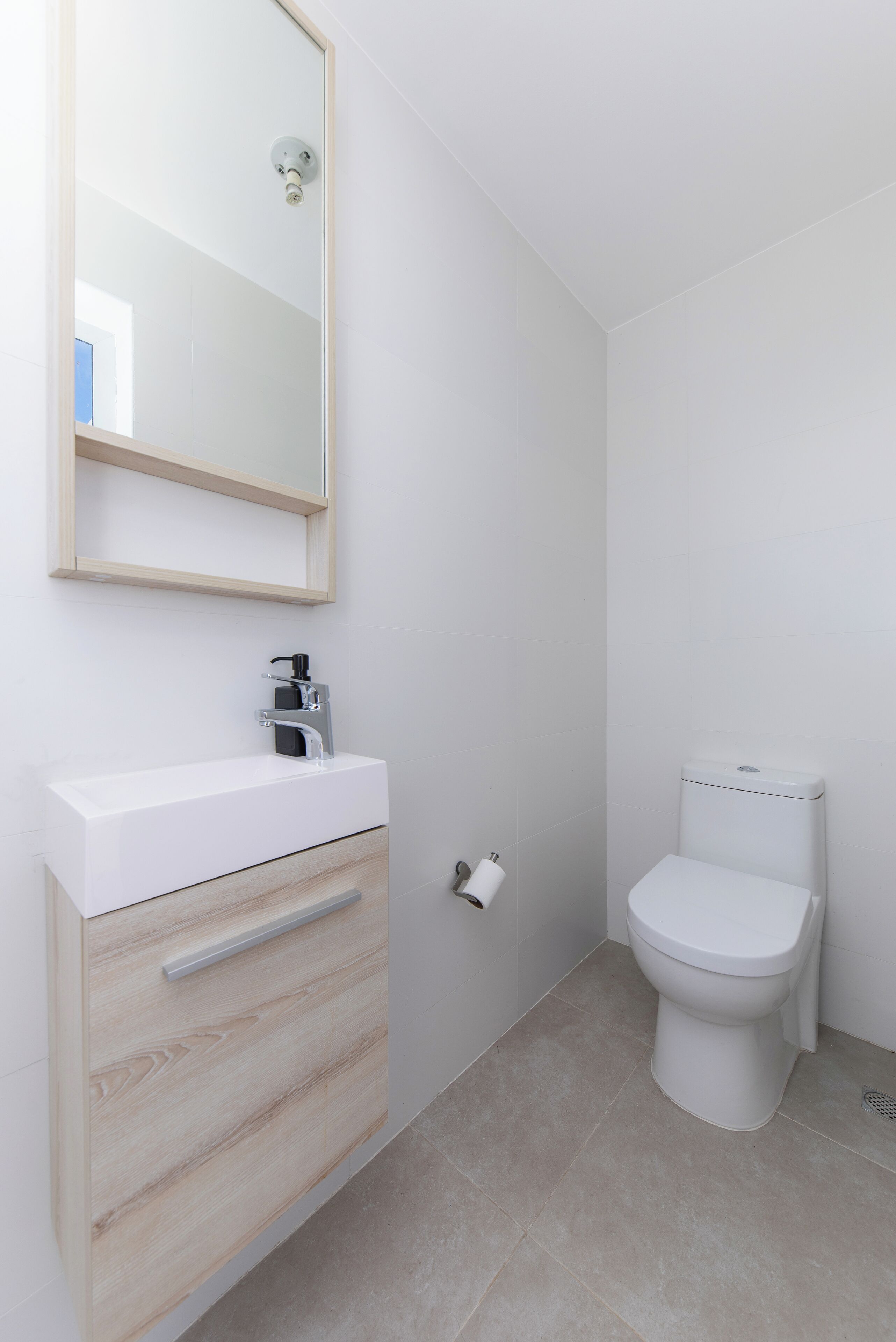A modern bathroom with a white sink, wooden cabinet, and a toilet.
