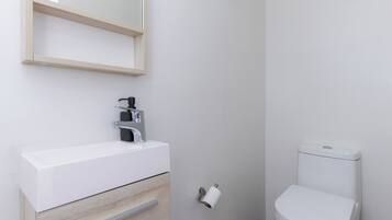 A modern bathroom with a white sink, wooden cabinet, and a toilet.