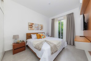 A bedroom with a bed, nightstand, TV, and a window with curtains. - Villa in Playa Mueva Romana – Steps from Beach! (San Pedro de Macorís)