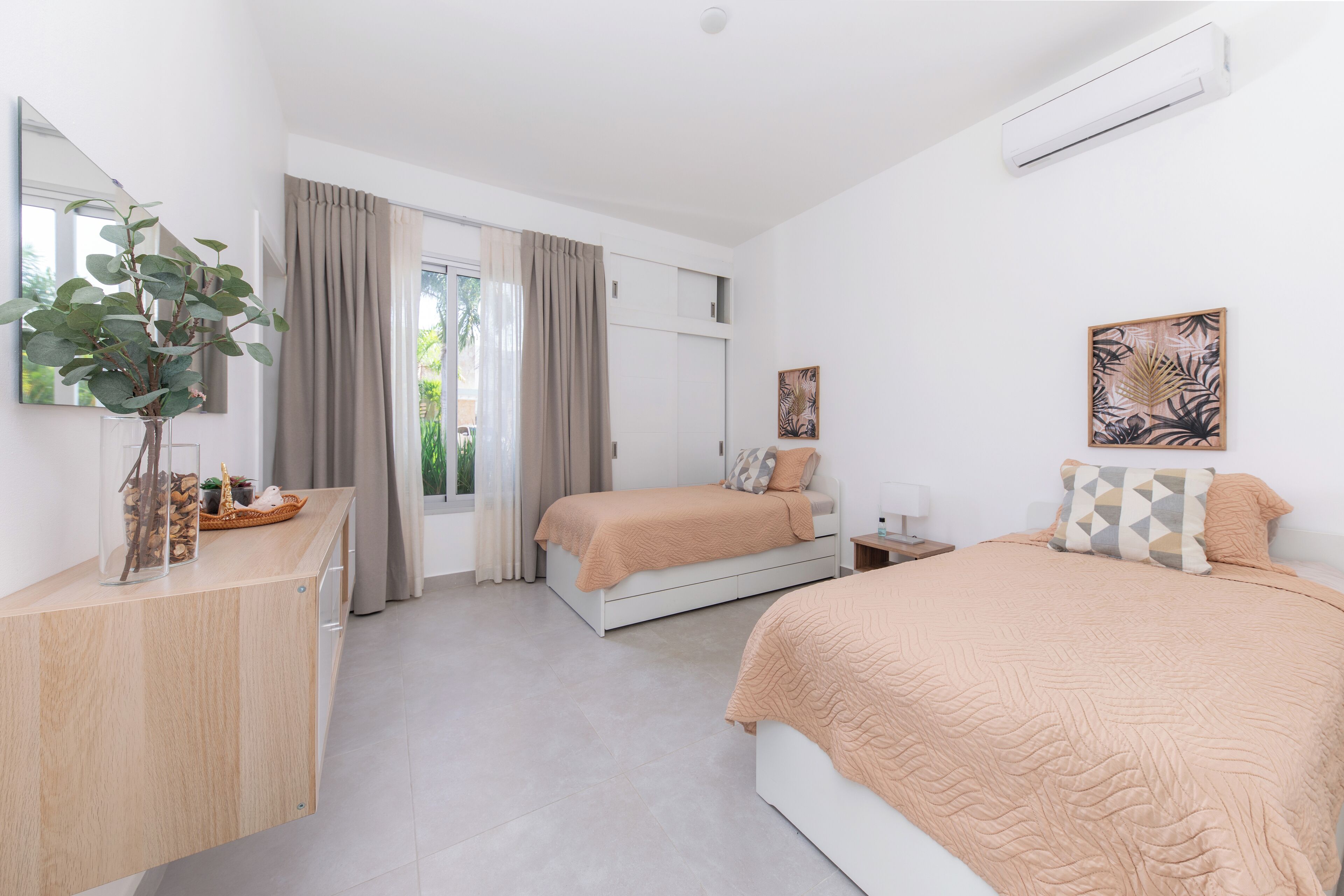 Een moderne slaapkamer met een groot bed, een kleiner bed, een bureau en een raam met gordijnen.
