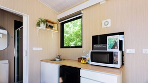 A compact kitchen with a microwave, a small sink, and a window with a view of greenery.