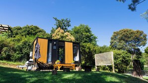 A compact wooden cabin with a deck, outdoor seating, and a large window.