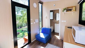 A modern room with a blue sofa, a kitchen area with a microwave, and a large window offering a view of a garden.