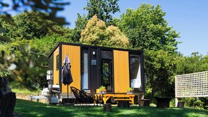 A small, modern cabin with a wooden exterior, a dining area with a table and chairs, and a covered outdoor seating area.