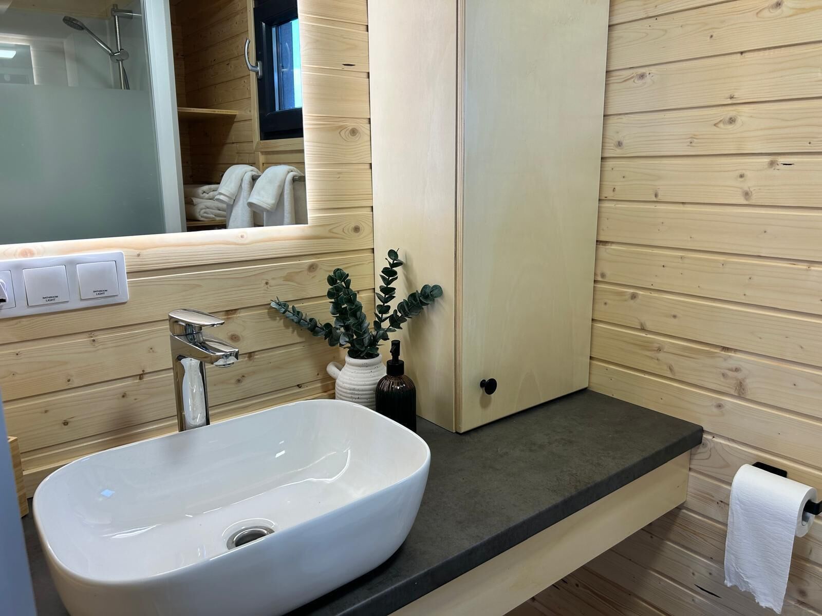 Een badkamer met een wit wastafel, een spiegel, een handdoekrek en een houten wand.